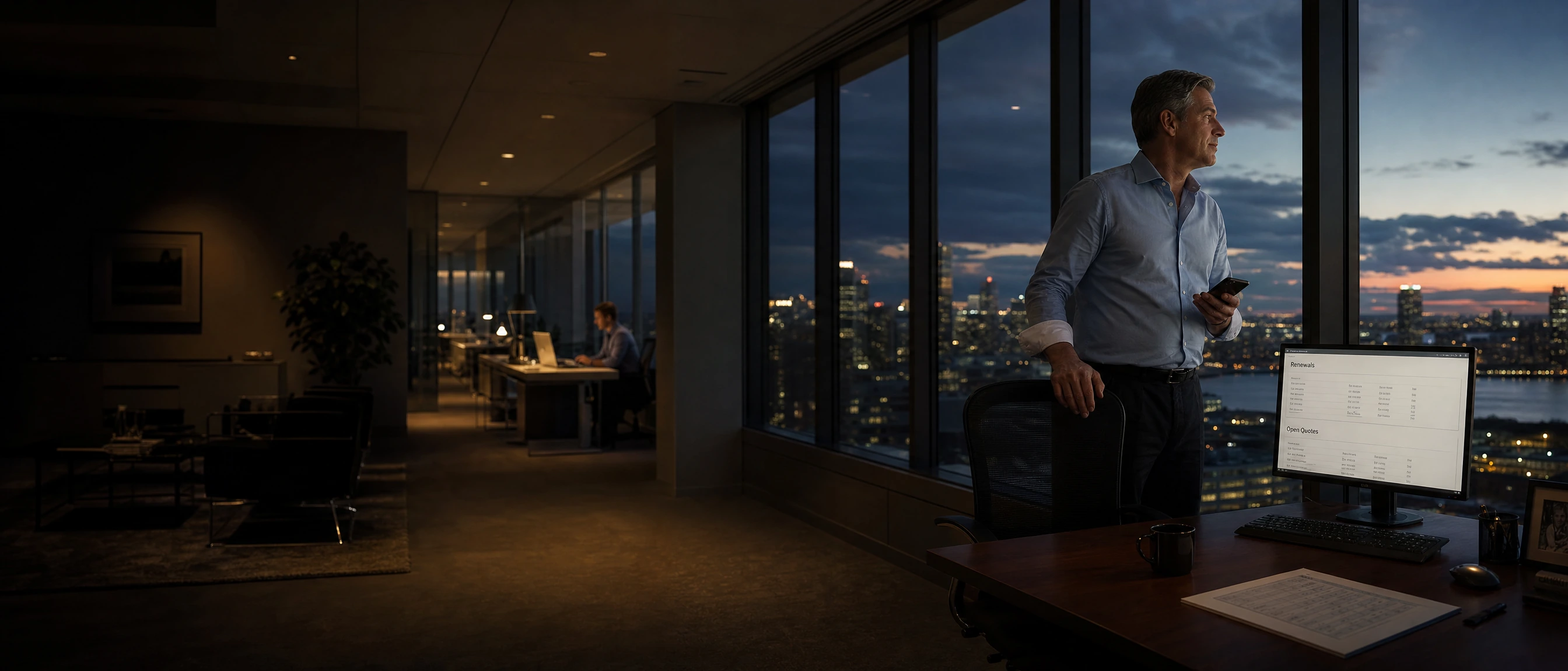The agency principal at the glass after a call, renewals and open quotes on the screen beside him